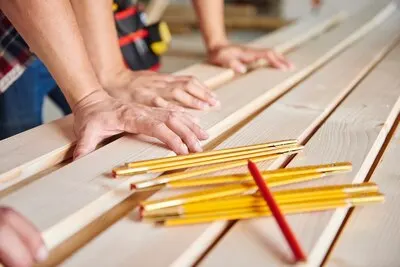 Younger and older carpenter measuring wooden planks