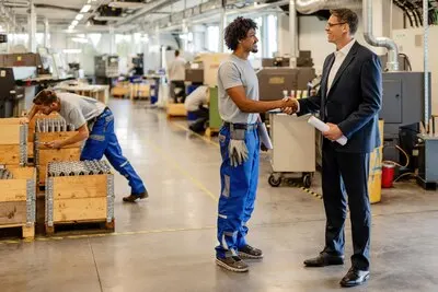 Happy black manual worker and engineer handshaking while greeting in industrial building