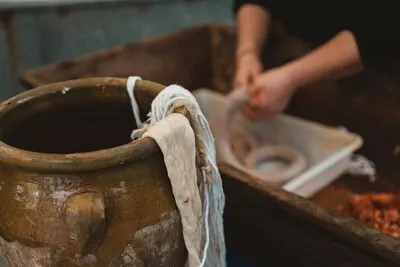 Closeup of fabric on a clay pot with a person preparing a kielbasa on the blurry