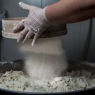 Side view dough with flour and sieve and human hand