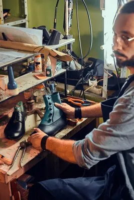 Experienced shoemaker is creating retro leather shoes at his comfortable workshop.