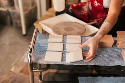 Female drying the white small tiles in workshop