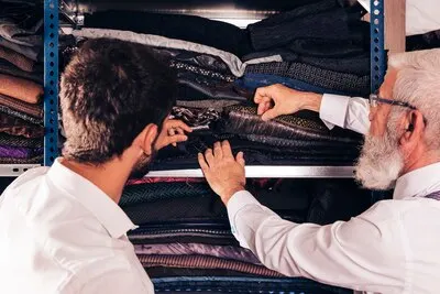 Close-up of man and male senior tailor selecting the fabric in the shelf
