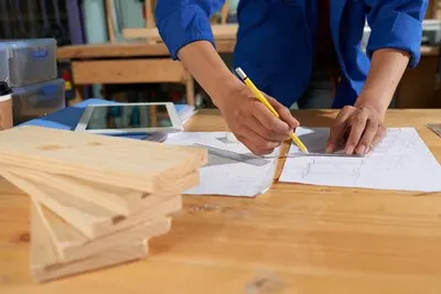Cropped man wearing blue overall drawing furniture on the sheet of paper